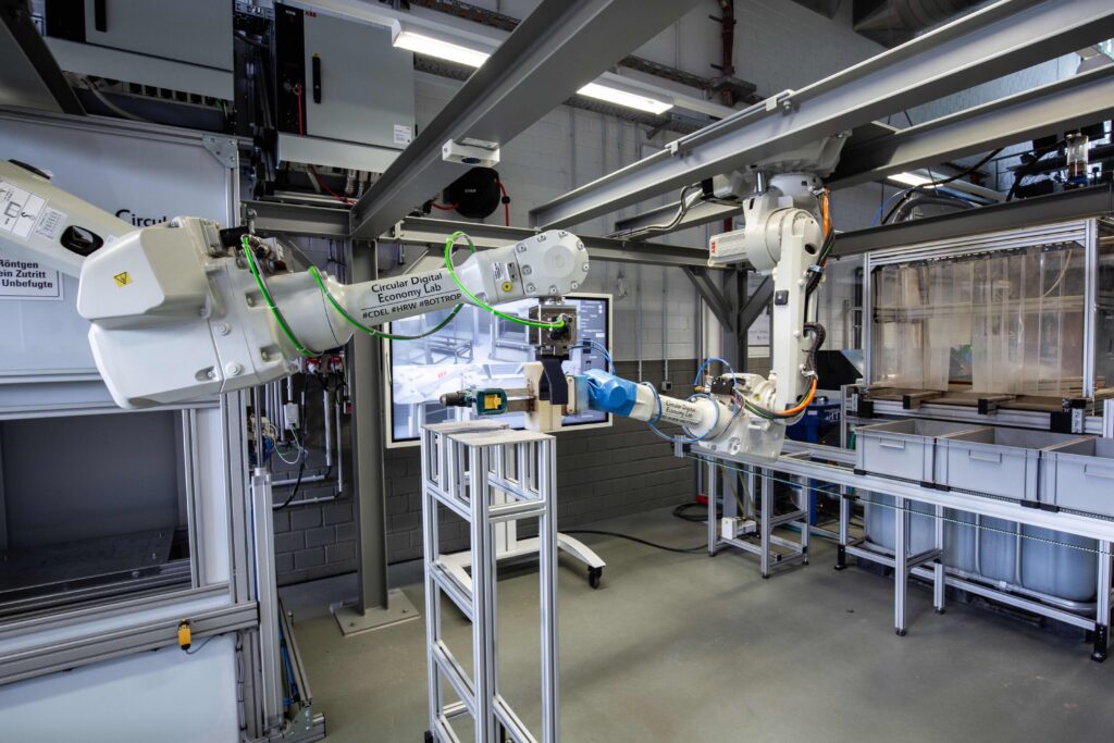 Materialrückgewinnung. Bild 3: Aufnahme aus dem CDEL: Nach der Datenerfassung übergibt Roboter A den Akkuschrauber an Roboter B für die Fraktionierung © Mike Duddek, Hochschule Ruhr West